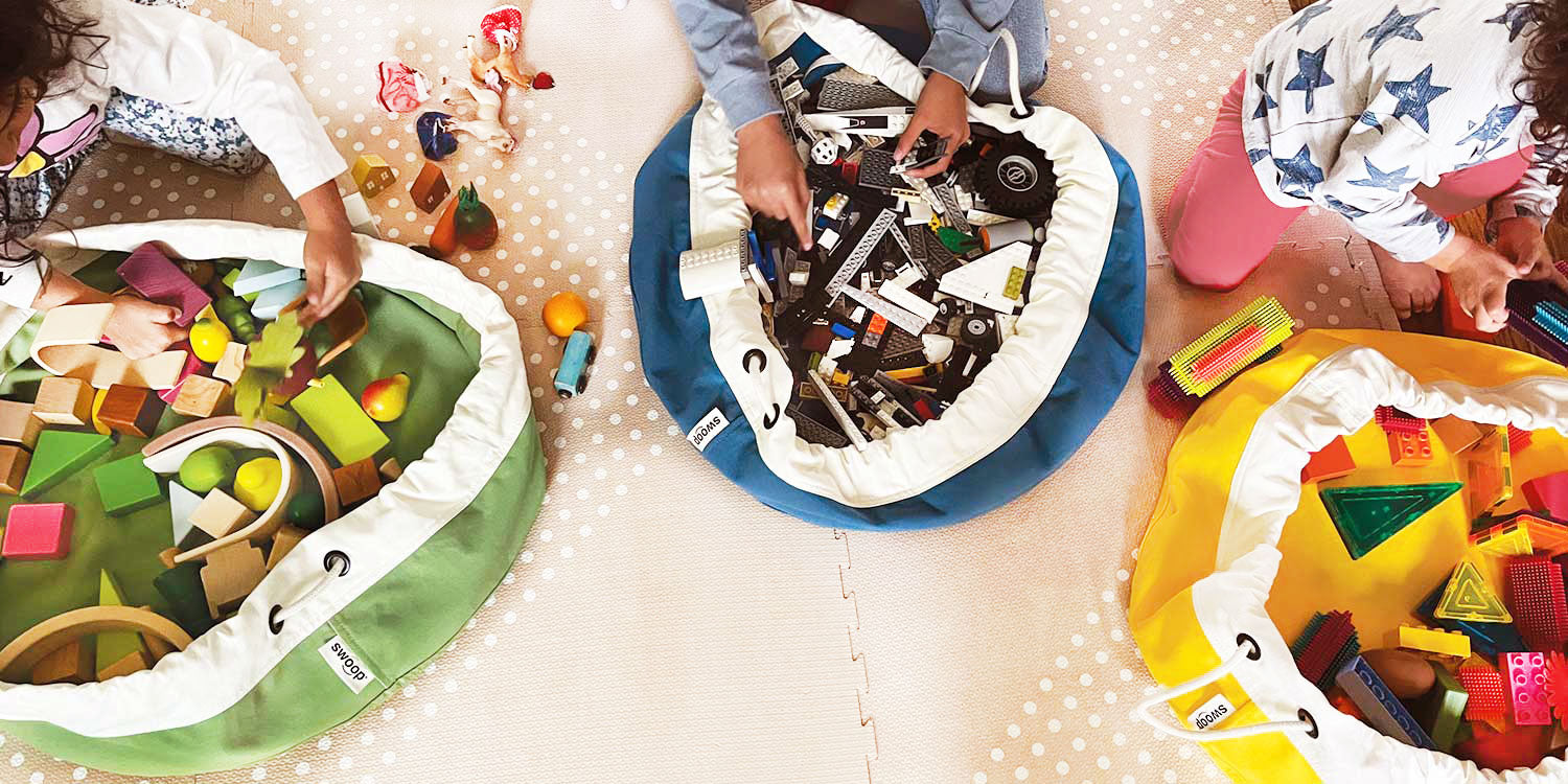 Children on floor playing with small toys like LEGO, wooden blocks and using a Swoop Bag to contain the mess - ideal storage for small toys